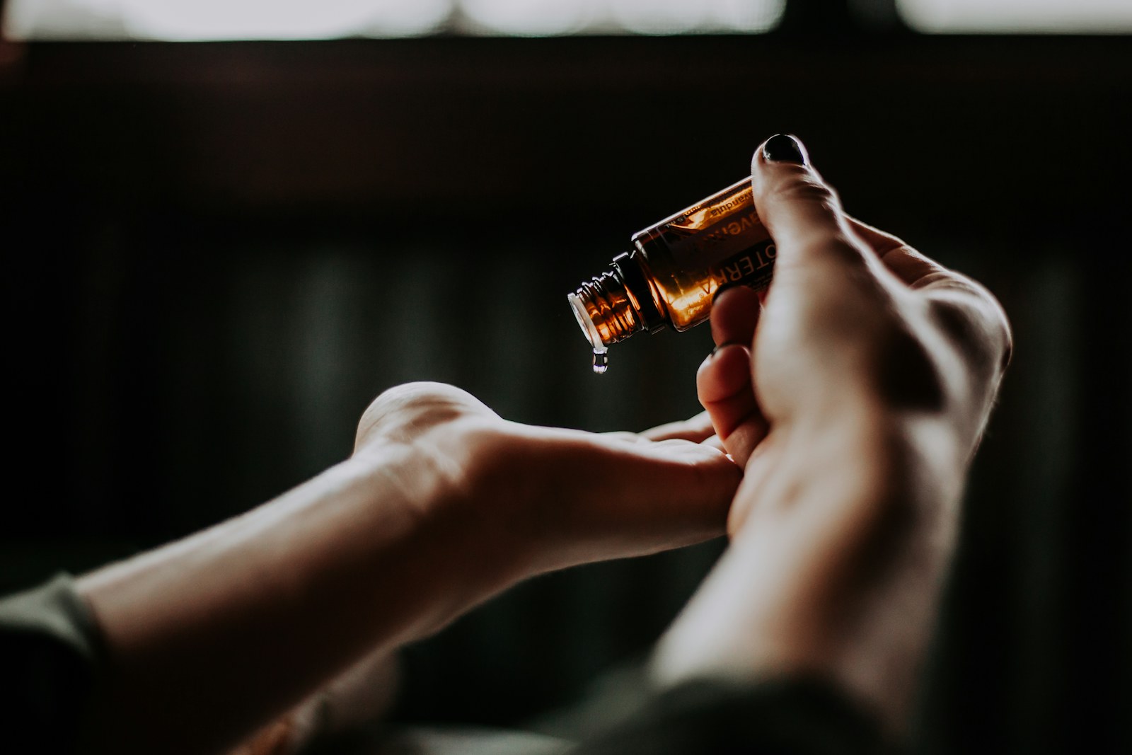 Hands holding a small amber skincare bottle in moody light