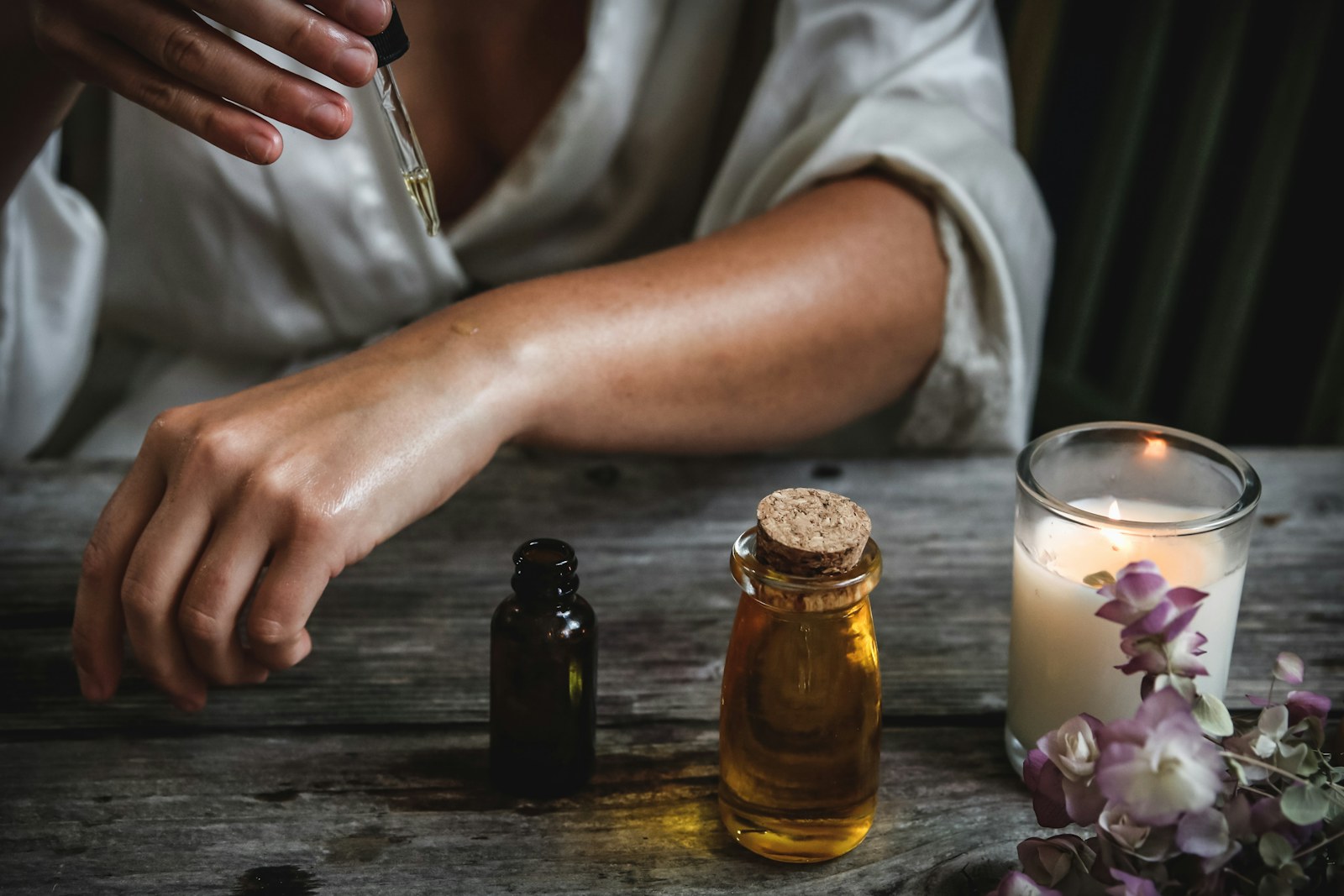 Hands resting beside an amber skincare bottle and candle in low light